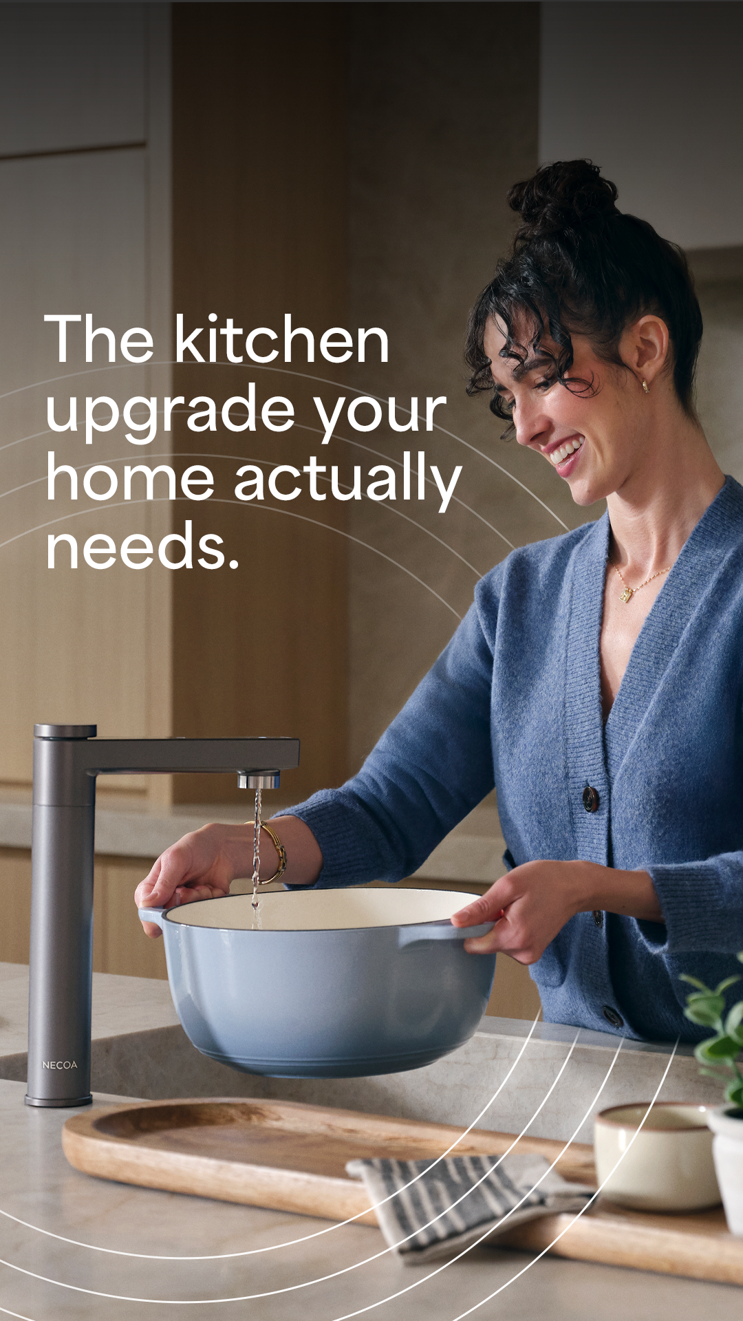 A woman with her hair in a bun smiles as she fills a light blue pot with water from a sleek, dark grey kitchen faucet. Text overlay reads "The kitchen upgrade your home actually needs."