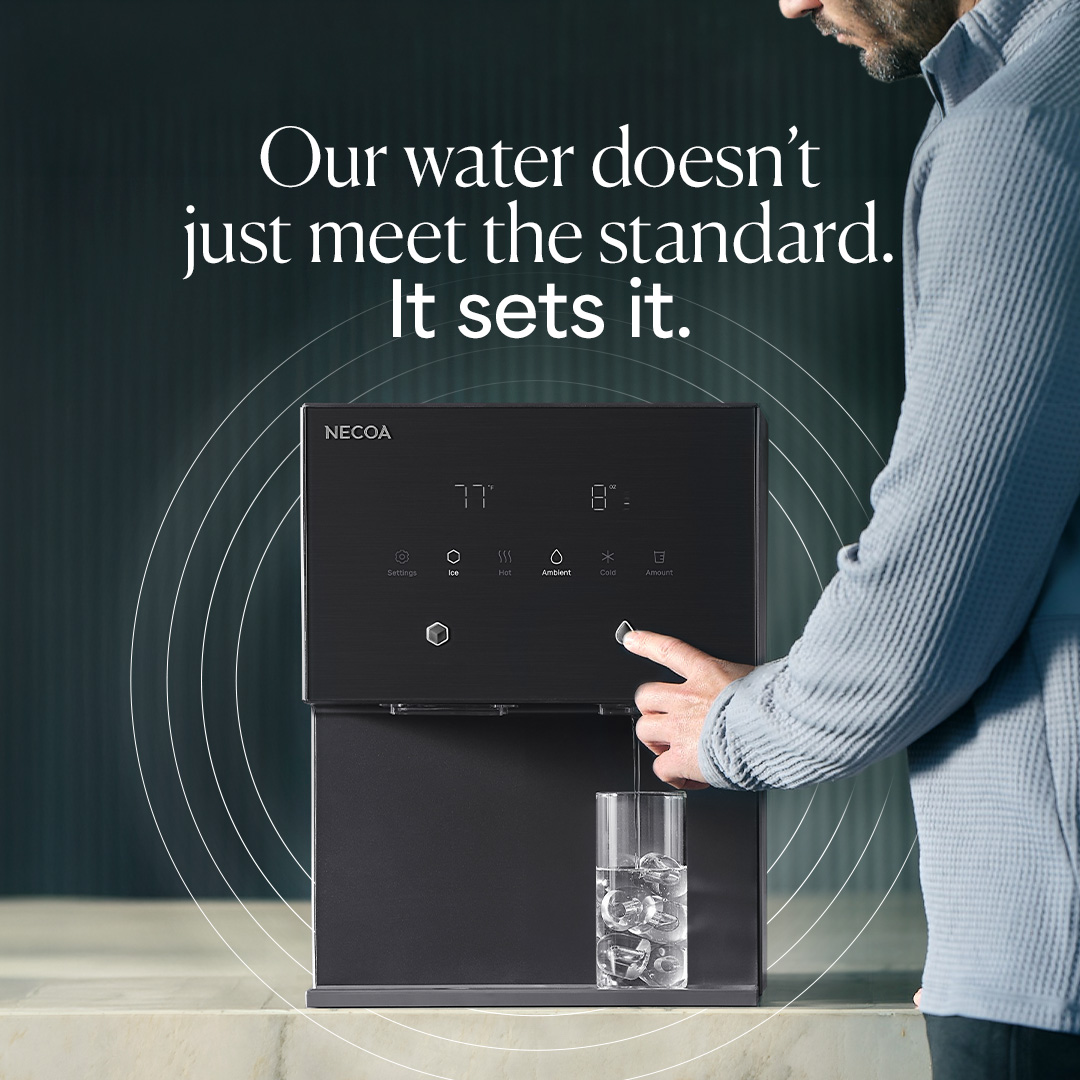 A man in a blue sweater presses a button on a black NECOA water dispenser, filling a glass with ice water. The dispenser has a digital display showing temperature and options for ice, hot, ambient, and cold water.